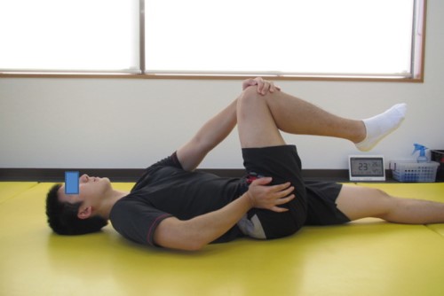 マットの上で股関節を動きやすくするための運動をしている男性